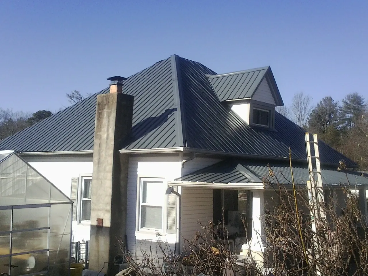 Dark blue standing seam metal roof on a white farmhouse with dormer — Slate & Tile Roof Repair by Roofing Brothers in Conneaut Lake