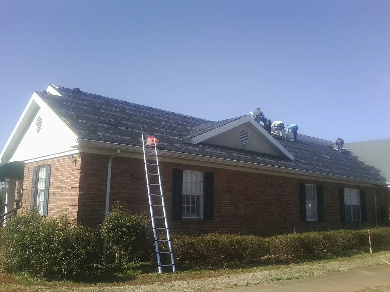 Crew tearing shingles off a brick ranch roof with a ladder set — Metal Roof Repair work by our crew in Conneaut Lake