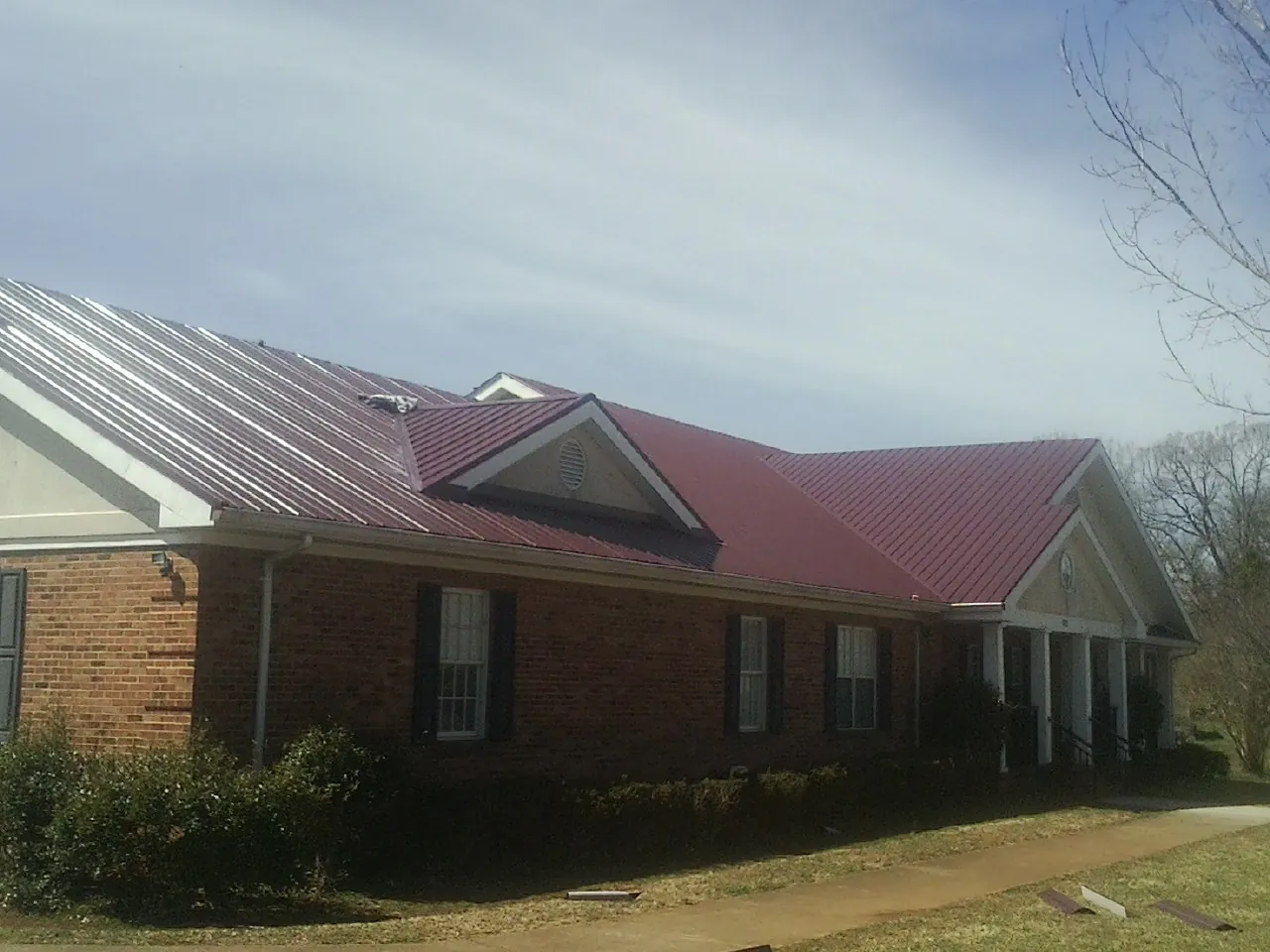 Red metal roof with gabled entries on a long brick building, from a Hail Damage Roof Repair job in Conneaut Lake