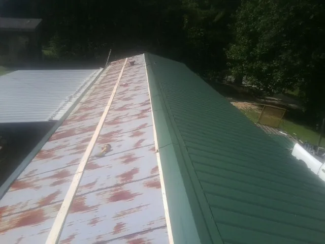 Old rusted panels beside newly installed green metal roofing — Wind Damage Roof Repair by Roofing Brothers in Conneaut Lake
