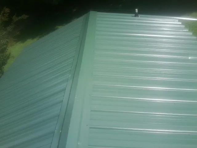 New green metal panels meeting at the ridge of a roof — Flat Roof Repair work by our crew in Conneaut Lake