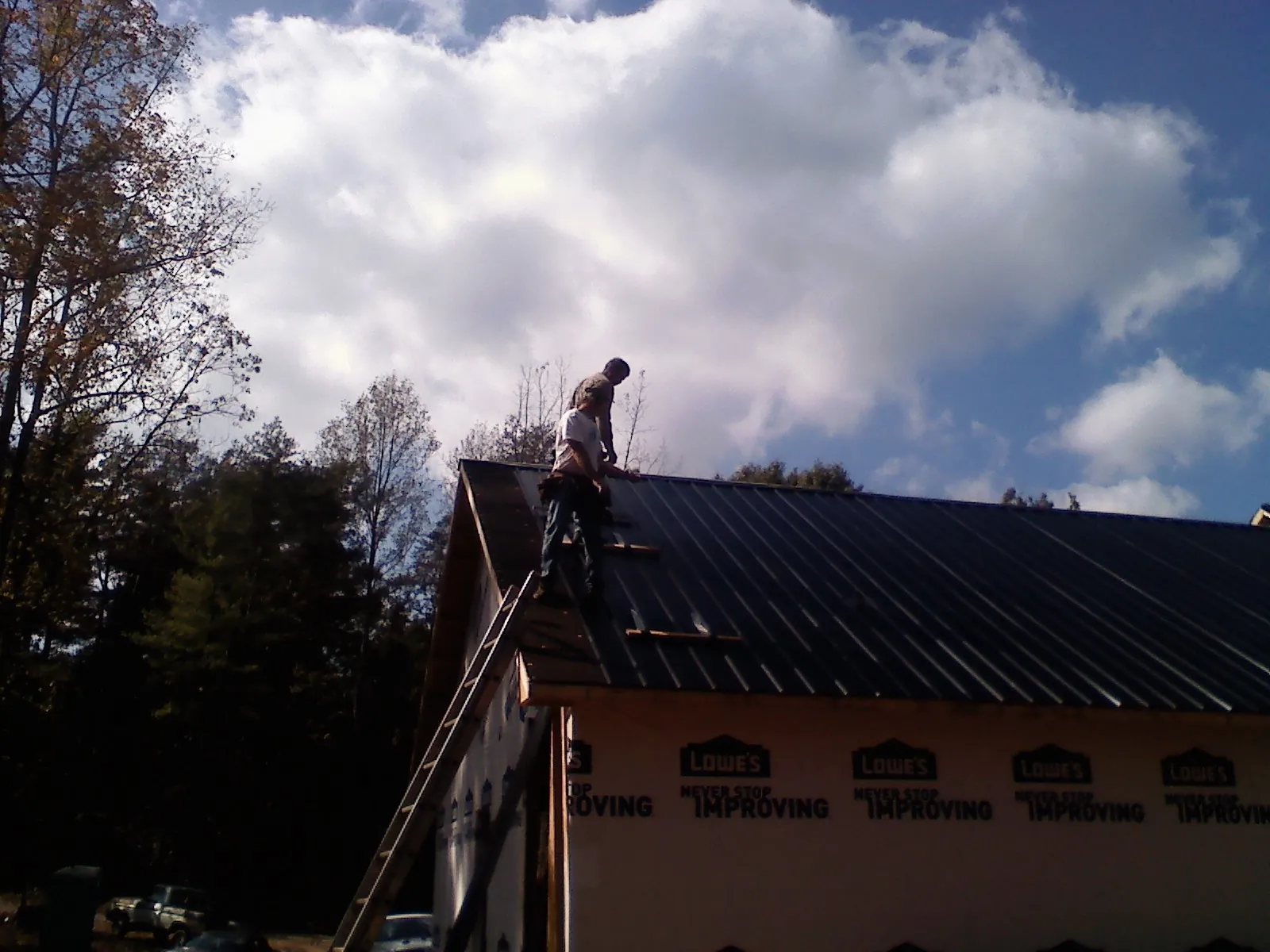 Roofer fastening dark metal panels high against a cloudy sky, from a Roof Inspection job in Conneaut Lake
