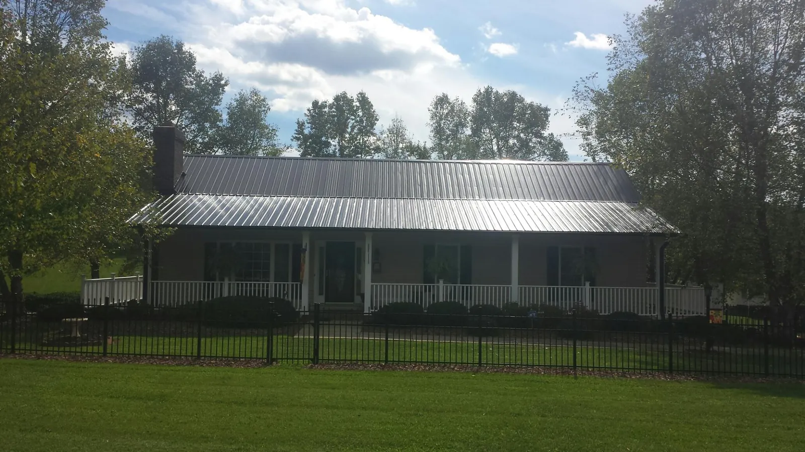 Gray metal roof on a brick ranch with a full width front porch — Gutter Guard Installation work by our crew in Conneaut Lake