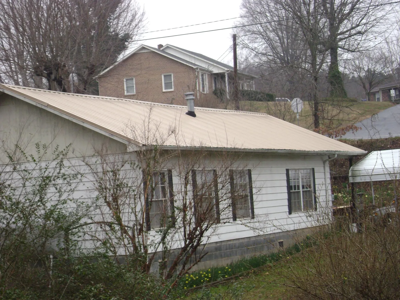 Tan metal roof on a white sided house set into a hillside — Commercial Roofing by Roofing Brothers in Conneaut Lake