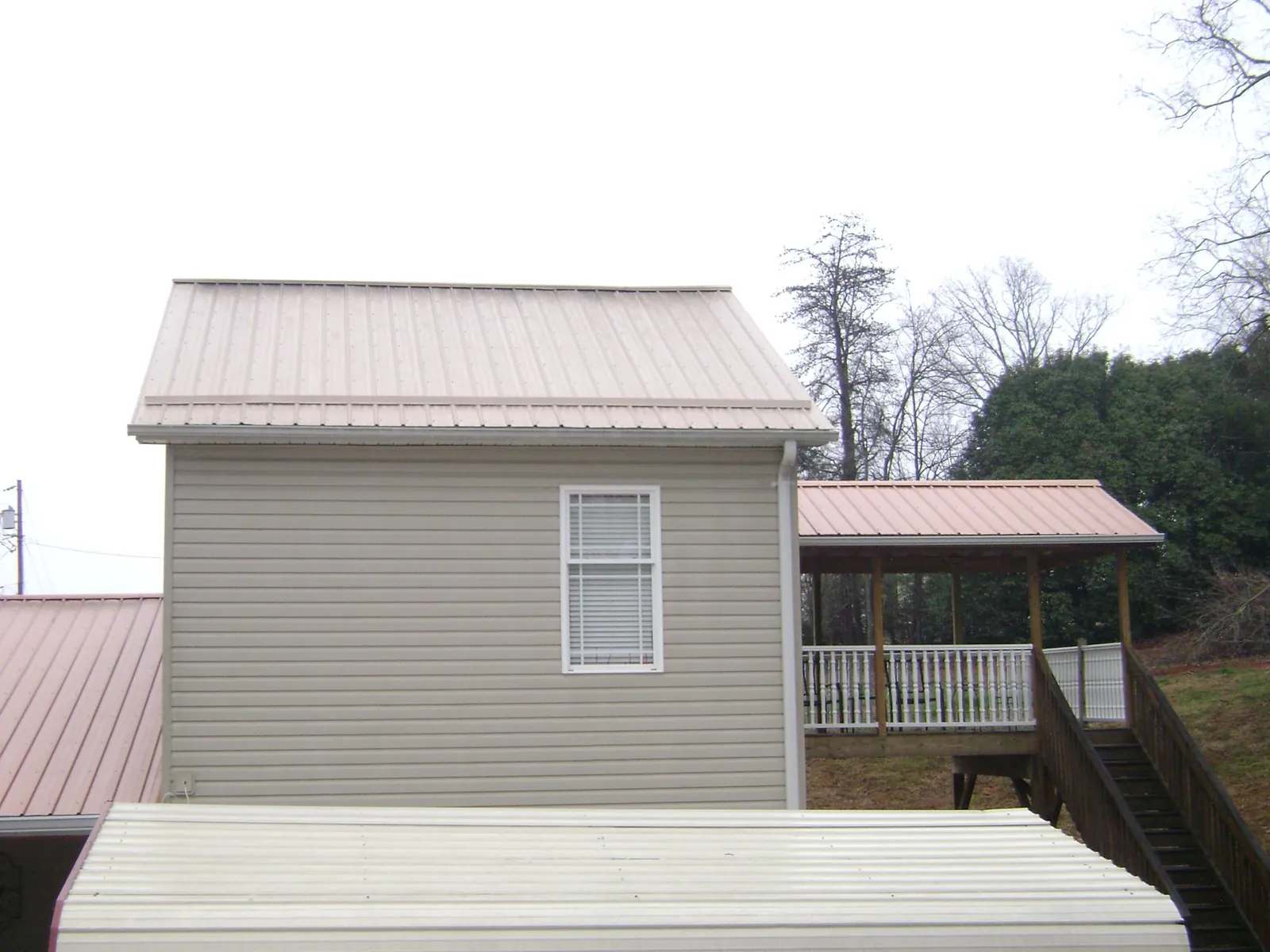 Tan metal roofs on a two story addition and attached porch, from a Roof Replacement job in Conneaut Lake